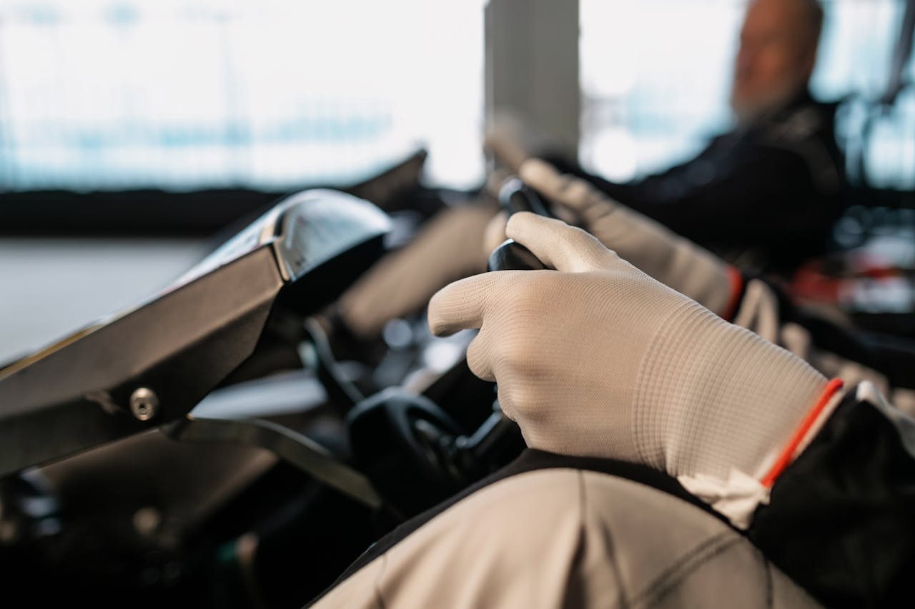 A focused shot of a racers gloved hands gripping the wheel of a go-kart, showcasing racing gear and motion.