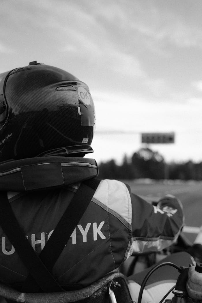 Back view of a driver in helmet and racing suit driving a go-kart on track.